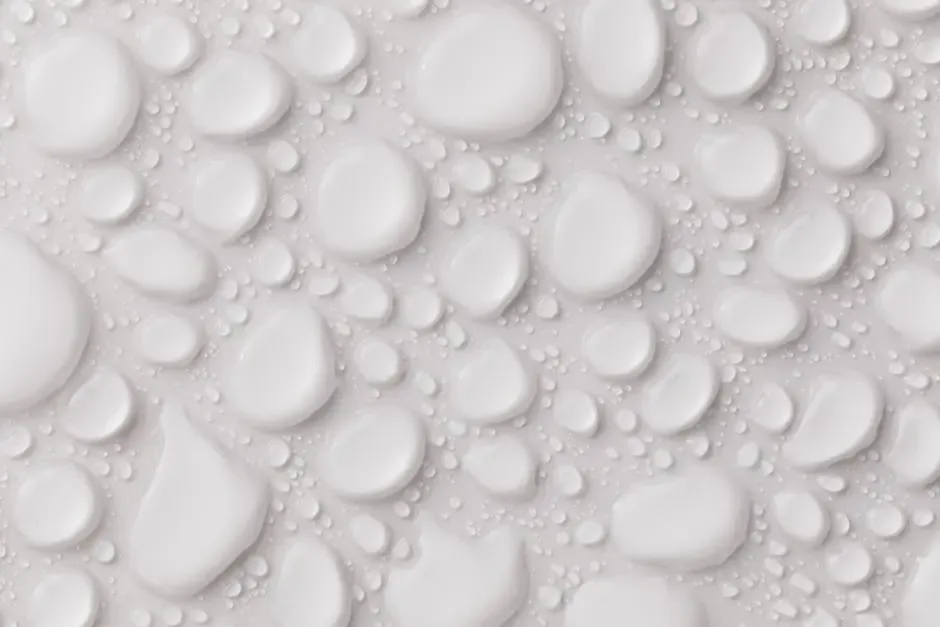 A close-up view of numerous glossy, white water droplets of varying sizes on a smooth, light gray surface, suggesting a context related to moisture management or leak prevention.