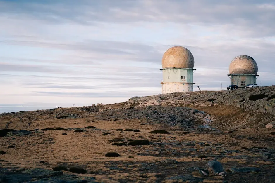 Two large radar domes sit atop a rocky, barren landscape under a cloudy sky, suggesting a remote location possibly related to surveillance or property protection.