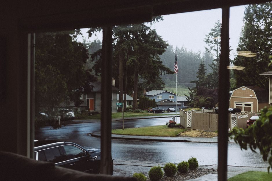 View of a quiet suburban neighborhood through a window on a rainy day, featuring a misty atmosphere.